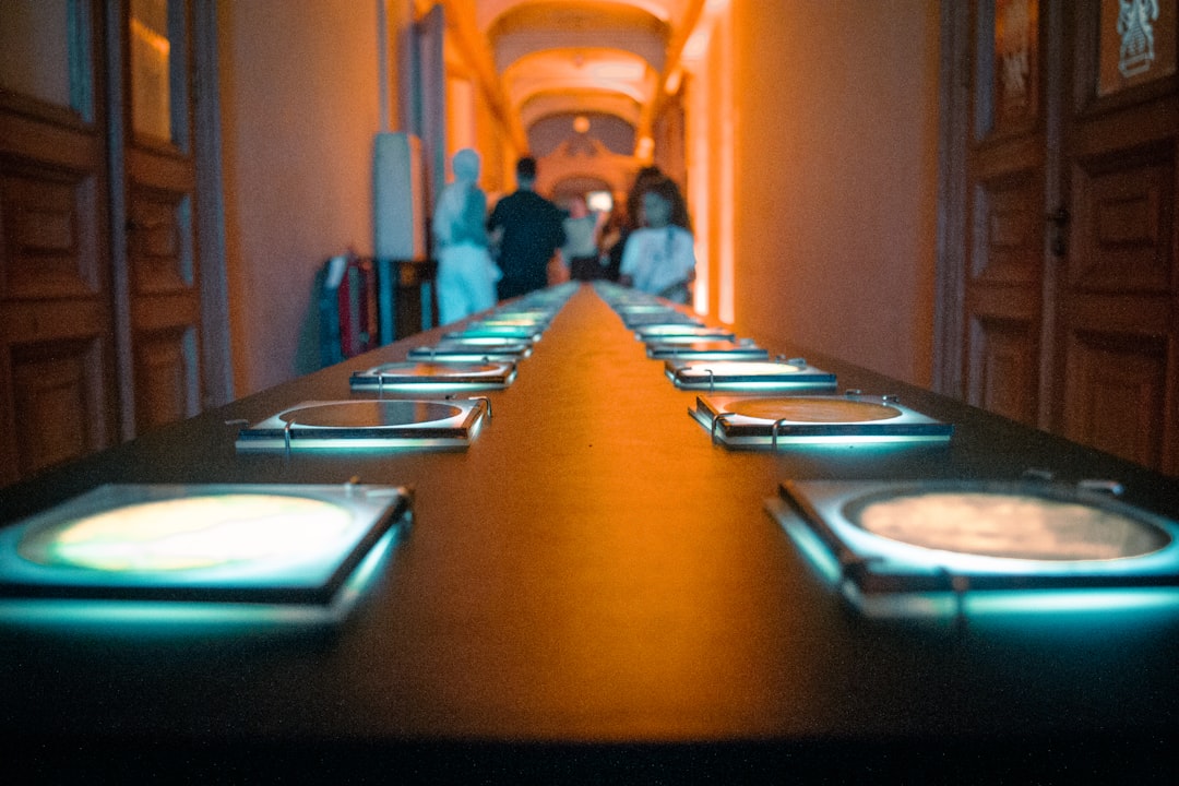 An indoor exhibit features a long, illuminated table showcasing various miniature world maps. Each section glows with soft blue light, guiding visitors through a visual exploration of global geography. The atmospheric lighting and symmetry create a futuristic museum experience.