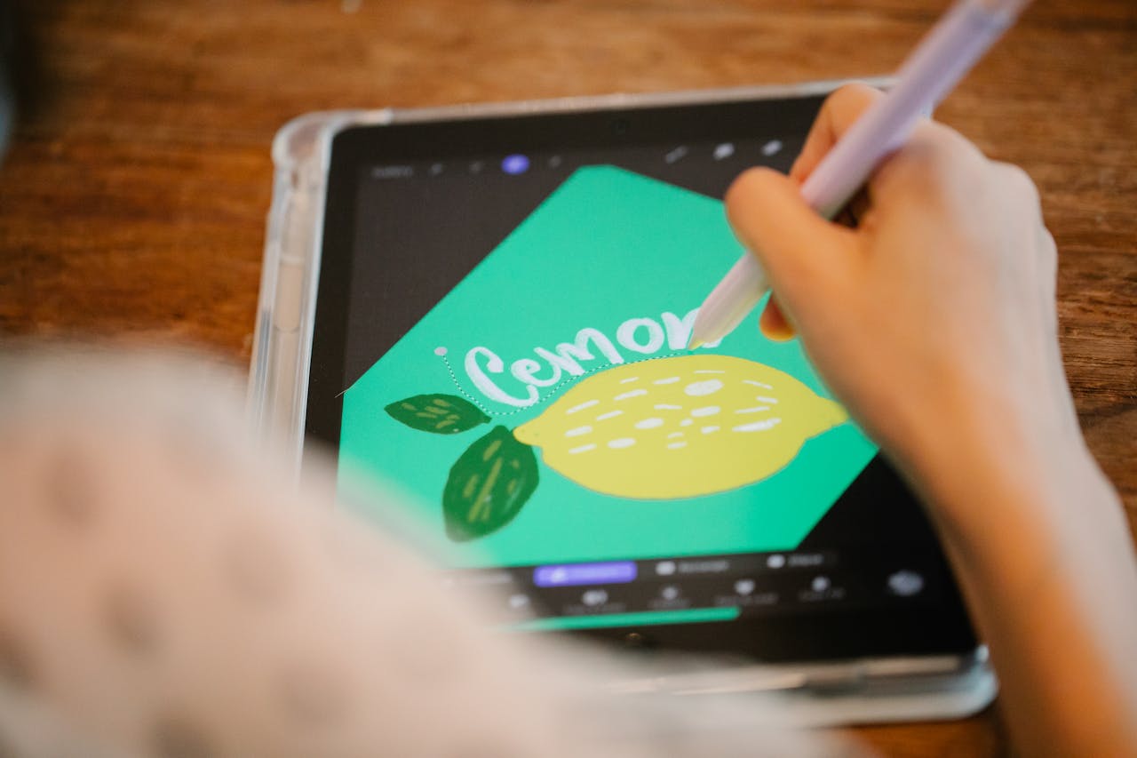 Close-up of a hand using a stylus to draw a lemon on a tablet screen.